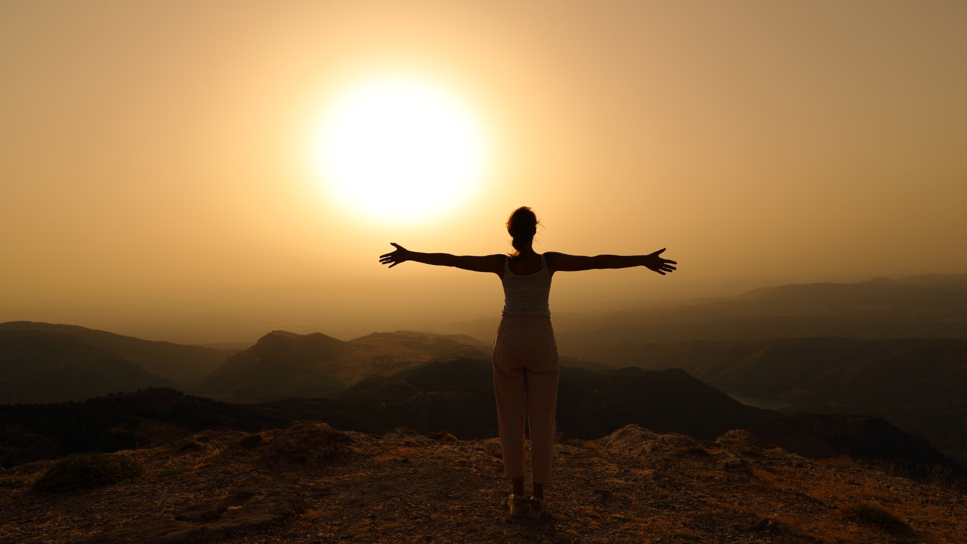 Nő a hegytetőn, karját széttárva a naplementében – a tudatos vezetés belső ereje és nyugalma.”