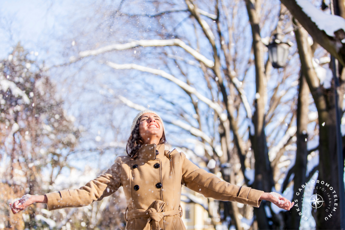 Mosolygó nő téli erdőben, kitárt karokkal a hóesésben – a jelenlét, felszabadultság és önmagunkhoz való visszatérés pillanata